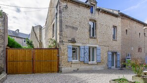 Un bâtiment en pierre avec une porte en bois, un petit jardin et un ciel dégagé.