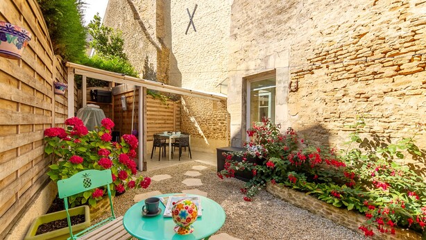Une cour avec une table en bois, des chaises et un espace salon abrité.