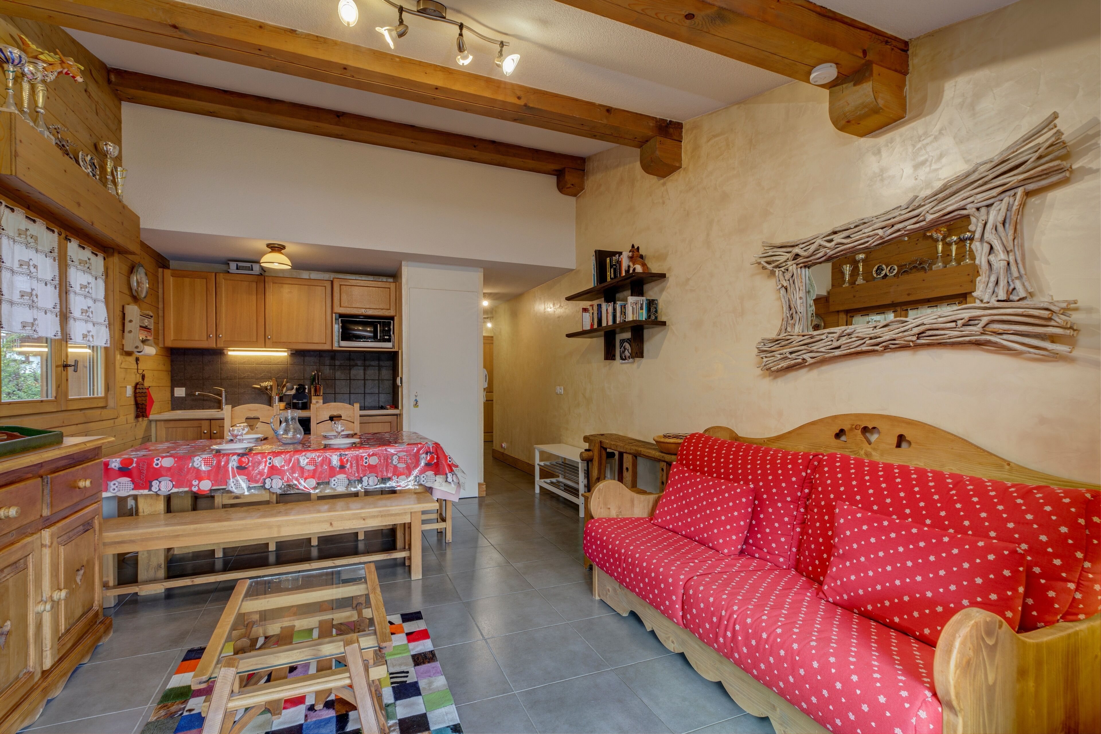 Une pièce chaleureuse avec une table en bois, un canapé rouge et un coin cuisine doté de meubles en bois et d’un four à micro-ondes.