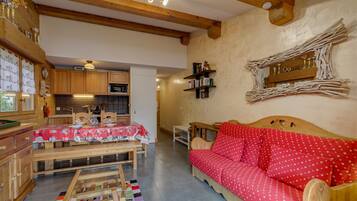 Une pièce chaleureuse avec une table en bois, un canapé rouge et un coin cuisine doté de meubles en bois et d’un four à micro-ondes.