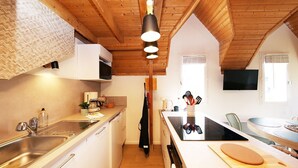 Une cuisine compacte avec un plafond en bois, un évier, une cuisinière et un coin repas comprenant une table et des chaises.
