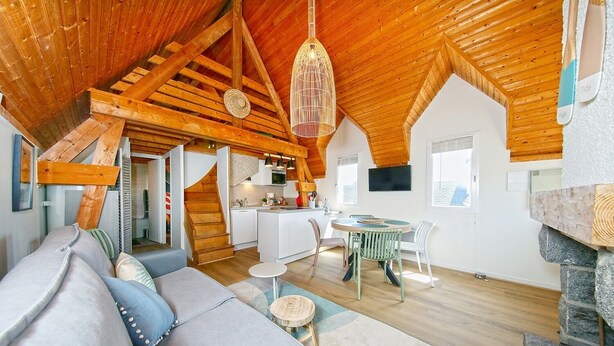 Un espace de vie chaleureux de style loft, avec un plafond en bois, un coin repas et une cuisine.