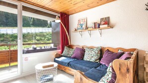 A wooden-framed sofa with cushions, a small round table, a floor lamp, and a window with a view of greenery. - Le Flocon de Pauline - Sur les pistes (Chamrousse)