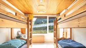 A room with two beds, wooden walls, a window with a view of a road and greenery, and a ceiling light. - Le Flocon de Pauline - Sur les pistes (Chamrousse)