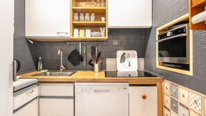 A modern kitchen with a dishwasher, oven, and a wooden shelf above the sink. - Le Flocon de Pauline - Sur les pistes (Chamrousse)
