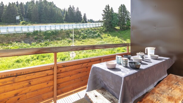 A balcony with a table set for dining, overlooking a forested area and a road. - Le Flocon de Pauline - Sur les pistes (Chamrousse)