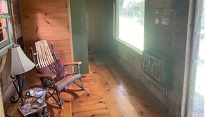 A cozy cabin room with wooden walls, a rocking chair, a table with a lamp, and a fireplace. - Hilltop Hideaway in the Nacoochee Village (Helen)