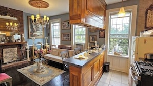 A kitchen with a central island, wooden cabinets, a chandelier, and a large window. - Luxurious Apartment at Colonial Townhouse (Queens)