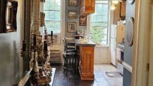 A narrow hallway with wooden flooring, a central column, and a hanging light fixture. - Luxurious Apartment at Colonial Townhouse (Queens)