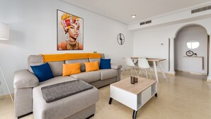 Un soggiorno moderno con un divano grigio, cuscini arancioni e blu, un tavolino da caffè e un quadro appeso al muro.