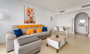 Ein modernes Wohnzimmer mit einem grauen Sofa, orange- und blauen Kissen, einem Couchtisch und einem Gemälde an der Wand.