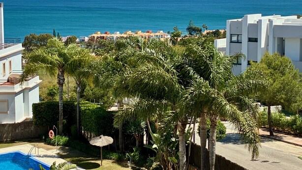 Quartiere residenziale con piscina, palme e vista sul mare.