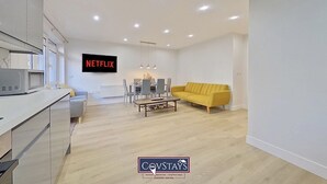 A modern living room with a yellow sofa, a dining table, and a TV displaying 'NETFLIX'. - Beauchamp House (Coventry)