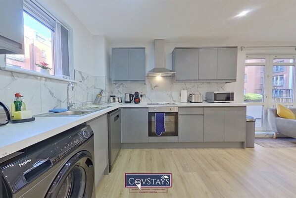 A modern kitchen with grey cabinets, a built-in oven, and a dishwasher. - Beauchamp House (Coventry)
