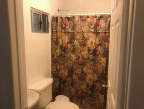 Un baño con inodoro, cortina de ducha con estampado floral y una pequeña ventana sobre el inodoro.