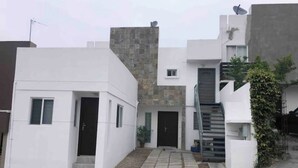 A modern residential building with a flat facade, a stone accent wall, and a small front yard with steps leading to the entrance. - A 10 min de la Garita de San Ysidro/zona Río (Tijuana)