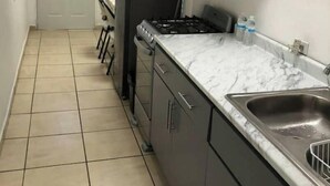 A narrow kitchen with dark cabinets, a gas stove, and a sink. - A 10 min de la Garita de San Ysidro/zona Río (Tijuana)