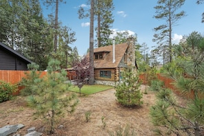 A log cabin with a stone chimney, surrounded by pine trees and a wooden fence. - The Hideout - Cozy Pet-friendly Cottage in Town (Idyllwild-Pine Cove)