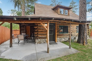 A log cabin with a covered patio, stone foundation, and a view of the surrounding forest.