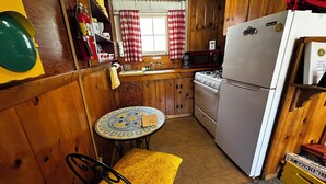 Una cucina compatta con pareti in legno, un piccolo tavolo rotondo, una panca gialla, un fornello, un forno a microonde e un frigorifero.