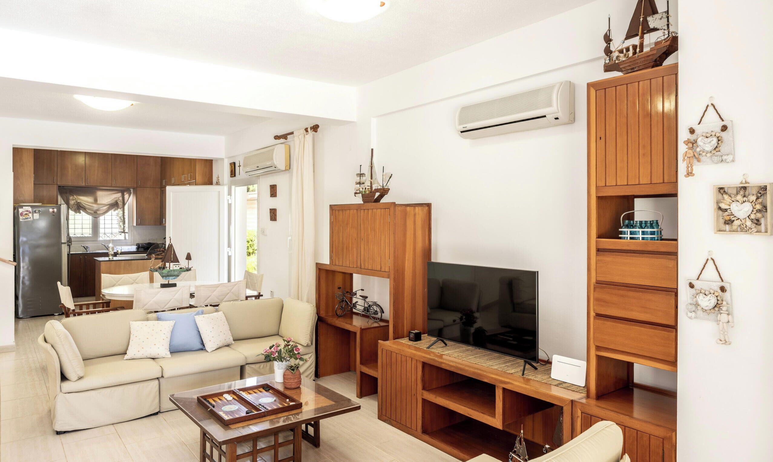 Ein Wohnzimmer mit Sofa, Couchtisch, Fernseher, Holzschrank und einer Küche im Hintergrund.