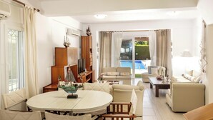 A living room with a round table, sofas, a TV, and a view of a swimming pool. - Protaras Apollon Seaside Villa (Protaras)