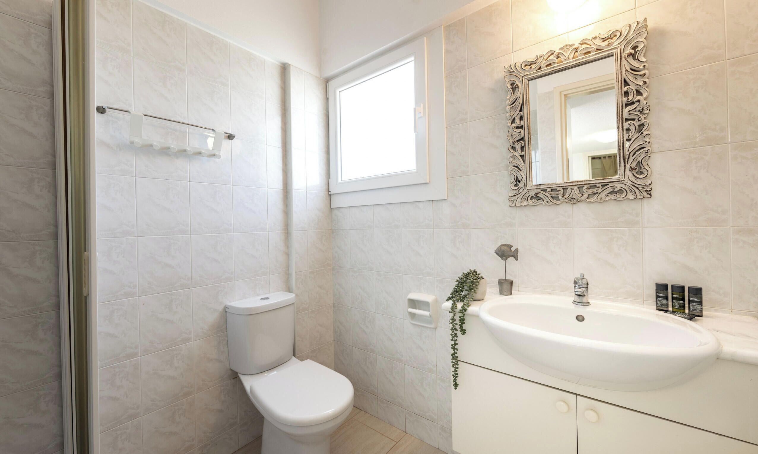 Une salle de bain avec des toilettes, un lavabo, un miroir et une fenêtre.