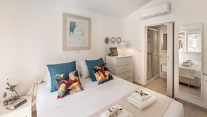 A hotel room with a bed, bedside table, nightstand, and a bathroom visible through an open door. - Protaras Apollon Seaside Villa (Protaras)