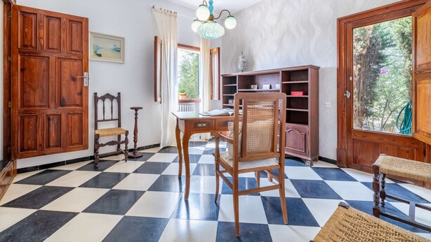 A room with a checkered floor, wooden furniture, a chandelier, and large windows with curtains. - Sa Tanca Llarga by Balearic Villas (Selva)