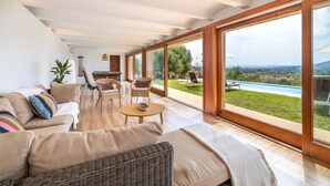 A spacious living room with a large window, a sofa, a coffee table, and a wicker chair. - Sa Tanca Llarga by Balearic Villas (Selva)
