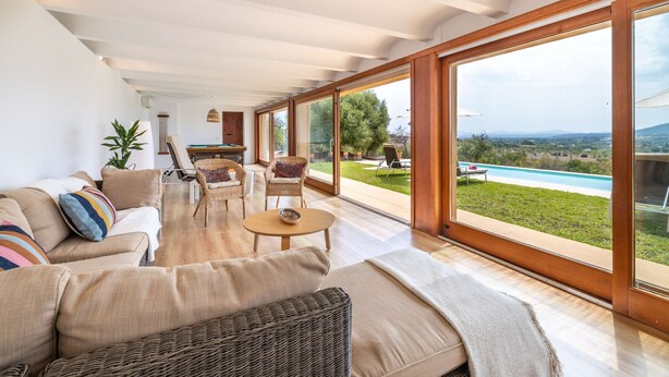 A spacious living room with a large window, a sofa, a coffee table, and a wicker chair.