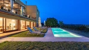 A modern house with a swimming pool, outdoor seating, and a view of the countryside.