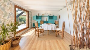 A dining area with a round table, wooden chairs, and a view through a large window.