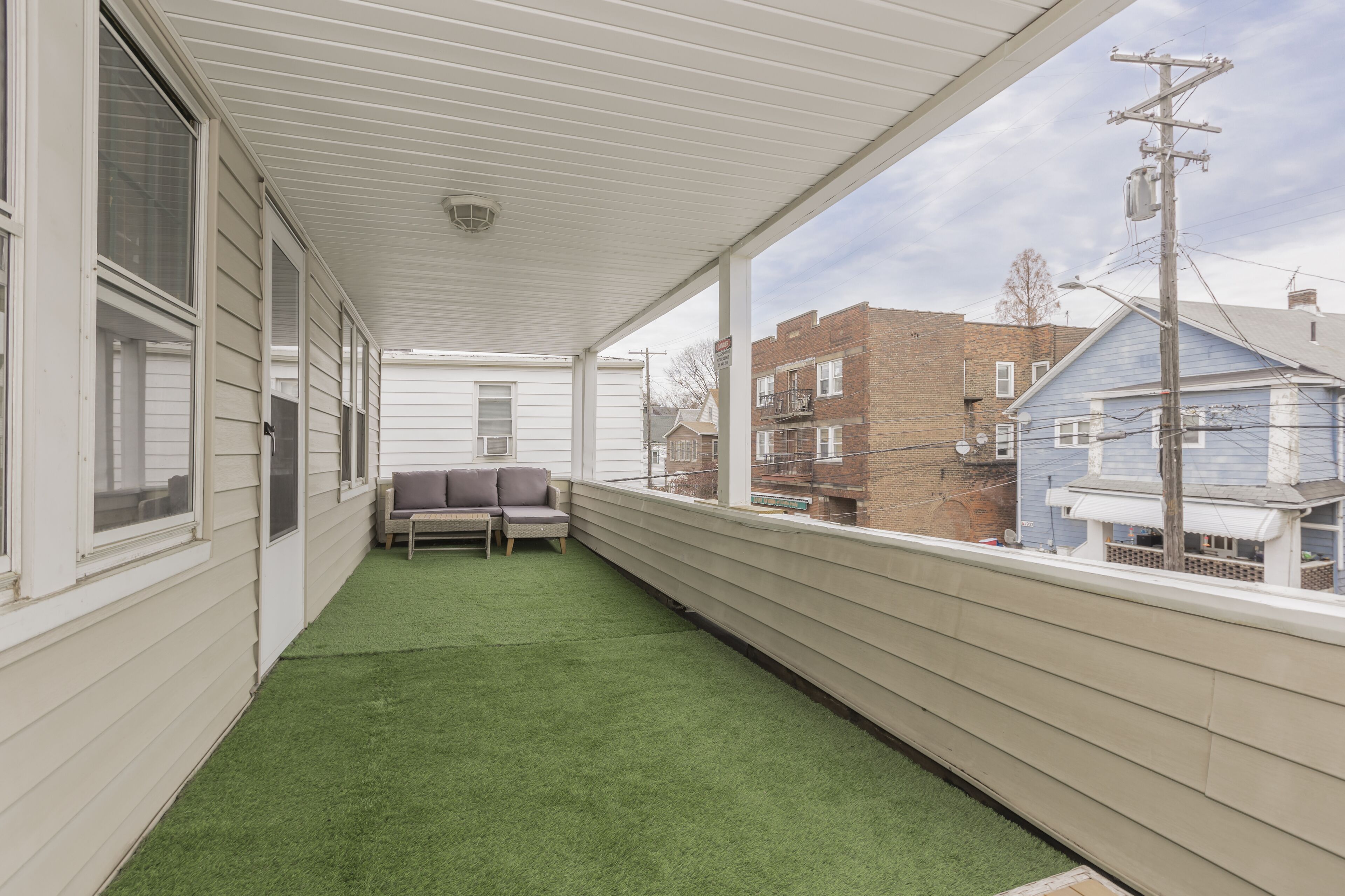 A covered balcony with artificial grass, a bench, and a view of neighboring buildings.