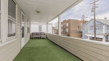 A covered balcony with artificial grass, a bench, and a view of neighboring buildings.
