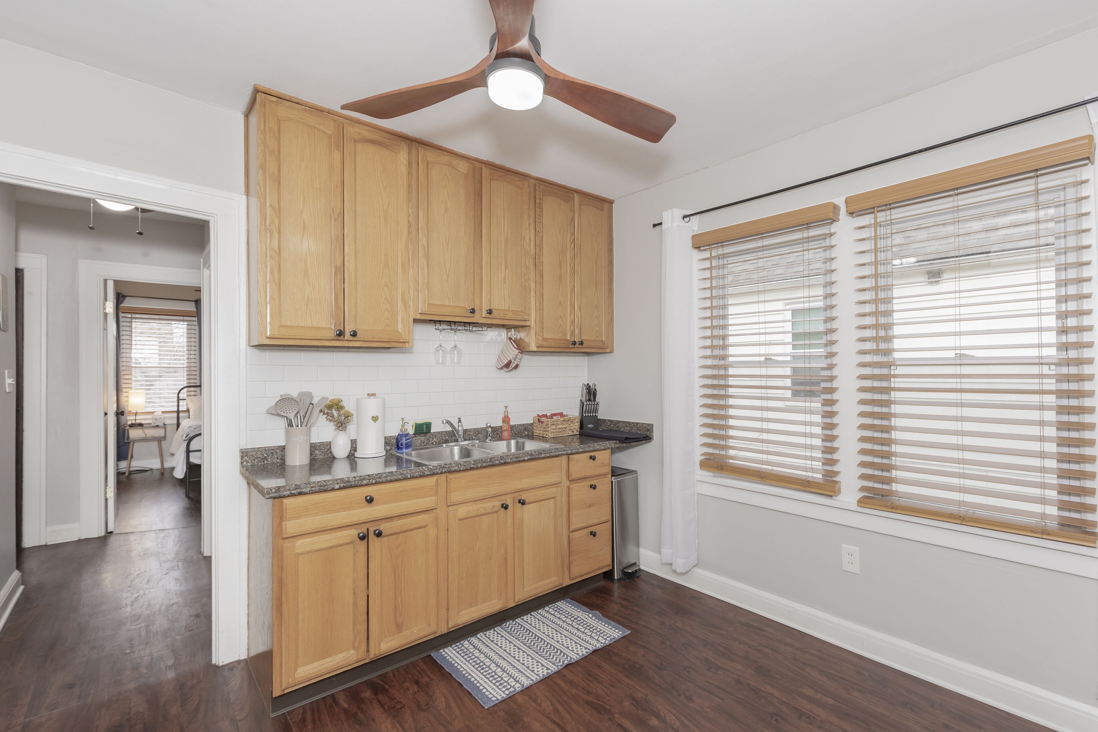 A kitchen with wooden cabinets, a granite countertop, a ceiling fan, and a window with blinds.