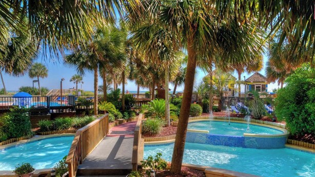 Een resort met meerdere zwembaden, een houten terras en weelderige begroeiing.