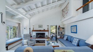 A spacious living room with a fireplace, a blue sofa, a checkered armchair, and a large window overlooking greenery. - Villa Pelago - Three Bedroom Villa, Sleeps 6 (Skopelos)
