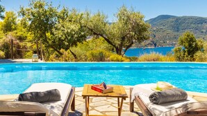 A poolside area with two sun loungers, a small table with a book, and a view of a body of water and hills in the background. - Villa Pelago - Three Bedroom Villa, Sleeps 6 (Skopelos)