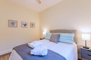 Quarto de hotel com uma cama, duas luminárias de cabeceira e três quadros na parede.