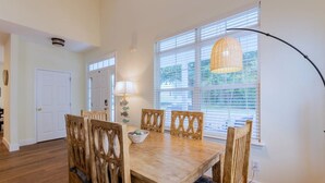 A dining area with a wooden table and chairs, a lamp, and a window with blinds. - Calypso Cottage in Old Town Bluffton. Single level home in the heart of historic Old Town (Bluffton)