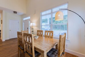 Uma área de refeições com mesa e cadeiras de madeira, uma luminária e uma janela com persianas.