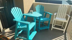 Ein Balkon mit türkisfarbenen Adirondack-Stühlen, einem kleinen Tisch und einem weißen Stuhl.