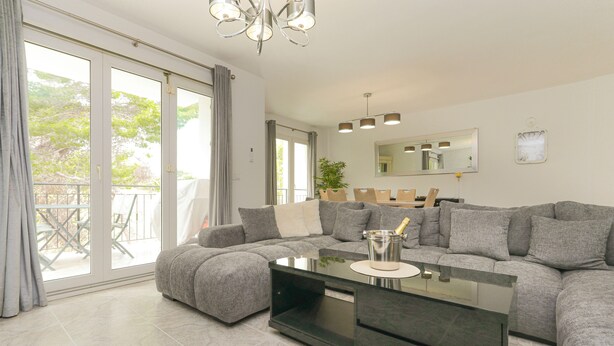 A modern living room with a sectional sofa, a glass coffee table, and a balcony with a view of trees. - Presidential suite in the Plaza of Villamartin. Front line Golf. No noise. (Villamartín)