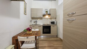 A compact kitchen with wooden cabinets, a microwave, and a small dining table with chairs. - Artist's Refuge by Mmega (Florence)