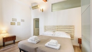 A bedroom with a bed, two bedside tables, a wall-mounted air conditioner, and a door. - Artist's Refuge by Mmega (Florence)