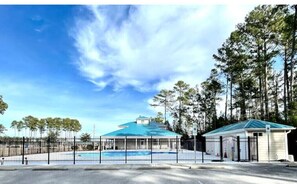 Surrounded by tall trees, this outdoor space features a swimming pool, a covered pavilion, and a small building.