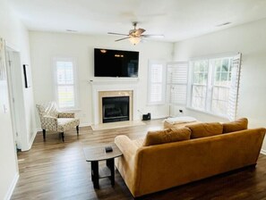 Relax in this spacious living room with a high ceiling, ceiling fan, and large windows.