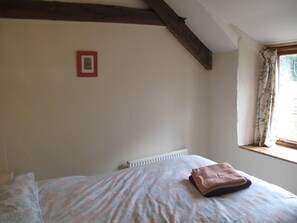 A bedroom with a bed, a window with curtains, a radiator, and a wooden ceiling beam. - Beautiful Large Rural Cottage Near Pencader (Pencader)