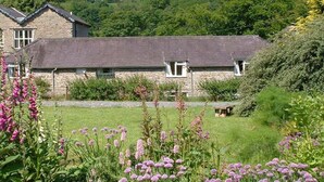 A stone building with a sloped roof, surrounded by lush greenery and flowering plants. - Beautiful Large Rural Cottage Near Pencader (Pencader)